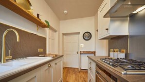 A modern kitchen with a stainless steel range hood, a double sink with a gold faucet, and wooden flooring. - The Jungle Nook: Romantic Hideaway with Log Burner (Berwick-upon-Tweed)