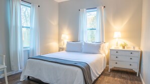 Een keurig opgemaakt slaapkamer met een groot bed, twee nachtkastjes met lampen, en een stoel.