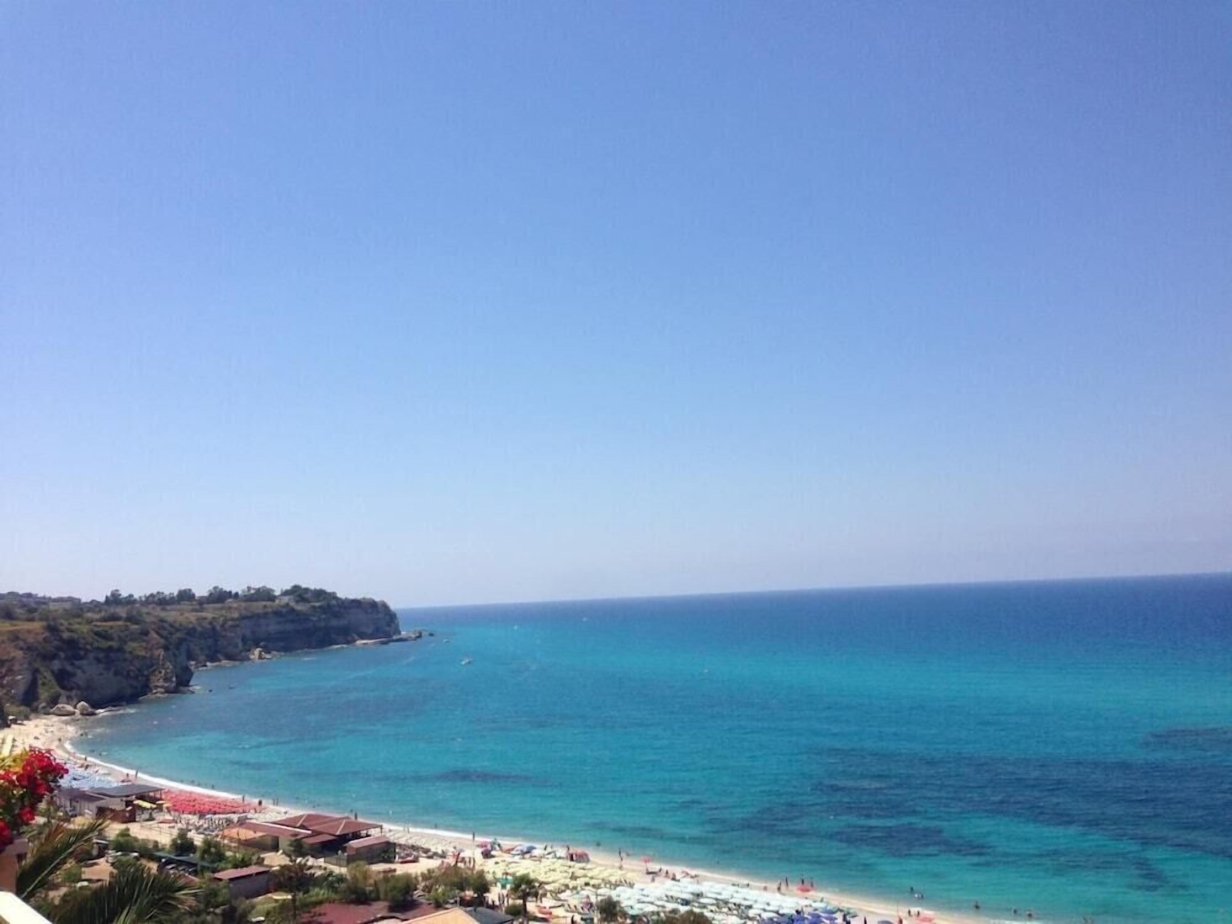 Vista sulla costa con spiaggia, mare cristallino e scogliere rocciose.