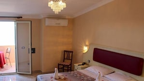 A hotel room with a bed, a chair, a nightstand, a chandelier, and a sliding glass door leading to an outdoor area. - Terrazzo Sul Mare Hotel (Tropea)