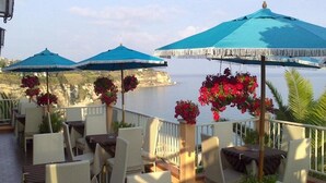 A terrace with outdoor seating, blue umbrellas, and red flowers. - Terrazzo Sul Mare Hotel (Tropea)