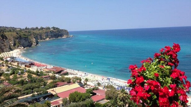 A coastal town with a beach, clear blue sea, and red flowers in the foreground. - Terrazzo Sul Mare Hotel (Tropea)
