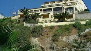 A multi-story hotel with balconies, situated on a hillside with palm trees. - Terrazzo Sul Mare Hotel (Tropea)
