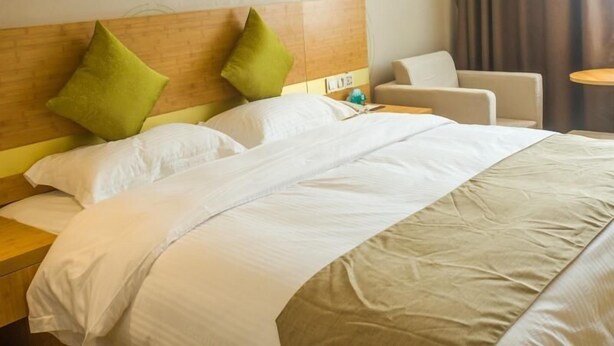 A hotel room with a large bed, two green pillows, a wooden headboard, a nightstand, a chair, and a small table. - Greentree Inn Hefei Lujiang County No.1 Jin Street Express Hotel (Hefei)