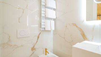 Un bagno con parete in marmo, pavimento in legno, WC bianco, bidet e lavabo con specchio.