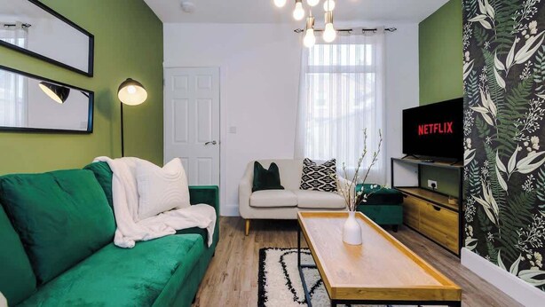 Ein Wohnzimmer mit einem grünen Sofa, einem weißen Sessel, einem Holztisch und einem Fernseher auf einem Schrank.