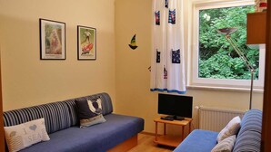 A cozy room with a blue sofa, a television on a small table, and a window with curtains. - Close to the beach and with sea views, apartment in a quiet, central location (Göhren)