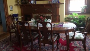 A dining room with a round wooden table, six chairs, a floral centerpiece, a fireplace, and a window with plants. - Harriet's Highlands Hideaway (Mount Pleasant)