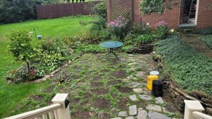 A backyard with a stone pathway leading to a green table, surrounded by various plants and a brick building. - Harriet's Highlands Hideaway (Mount Pleasant)