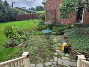 Enjoy outdoor dining or relaxation in this serene garden area with a table and chair, surrounded by lush plants and flowers.