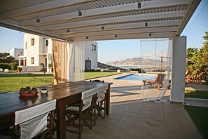 An outdoor patio with a pool, dining area, and a view of a mountain and sea.