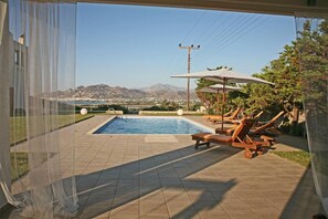 A pool area with a view of mountains, a pool, and lounge chairs.