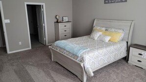 Una camera da letto con un letto, un comodino, una cassettiera e una porta che dà su un'altra stanza.
