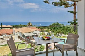 A balcony with a table and chairs, overlooking a pool and a view of the sea and buildings. - Ionian Aura (Akrotiri)