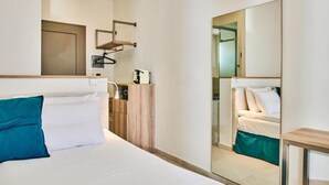 Habitació d'hotel amb un llit gran, un taulell de fusta, un mirall i una taula petita.