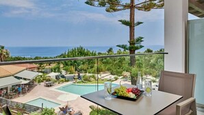 Un balcó amb taula preparada per a dinar, amb vista a una piscina i vegetació abundant, i una vista clara de l'oceà al fons.