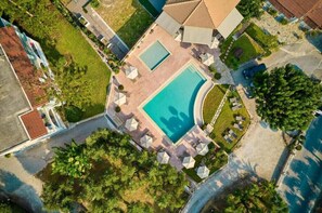 An aerial view of a resort with a central swimming pool, multiple lounge areas, and surrounding greenery. - Ionian Aura (Akrotiri)