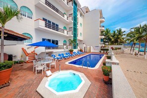 A hotel pool area with a hot tub, lounge chairs, and a staircase leading to the upper floors. - WIVC Casa de la Playa Condo - Literally on the Beach with Swimming Pool & Jacuzzi (Puerto Vallarta)