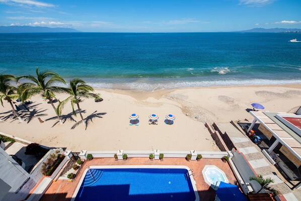 A beach view with a pool, palm trees, and umbrellas. - WIVC Casa de la Playa Condo - Literally on the Beach with Swimming Pool & Jacuzzi (Puerto Vallarta)