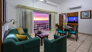 Una sala de estar con sofá, sillas, mesa y televisor. Se ve una vista del atardecer por la ventana.