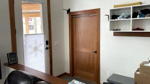 Una habitación con puerta de madera, un escritorio con computadora, una silla y un estante con cajas.