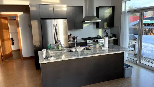 Una cocina moderna con electrodomésticos de acero inoxidable, una isla grande con un lavamanos y una puerta corrediza de vidrio que da a un área exterior nevada.