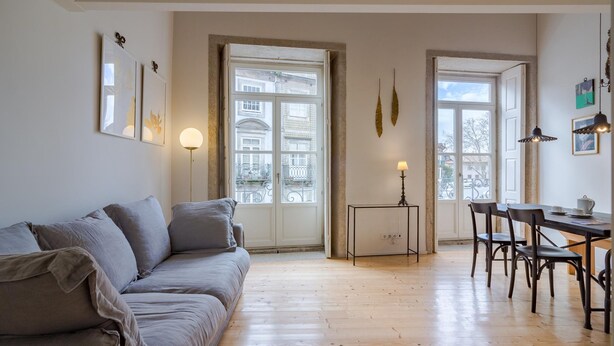 A modern living room with a grey sofa, wooden flooring, and large windows offering city views. - Porto Vitoria 5 in Oporto (Porto)