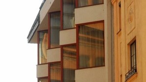 A multi-story building with a modern facade, featuring a series of rectangular windows and a prominent red flag on the corner. - Hotel Orion Varkert (Budapest)