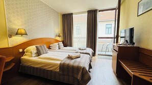 Habitación de hotel con dos camas, televisión, escritorio y balcón con cortinas.