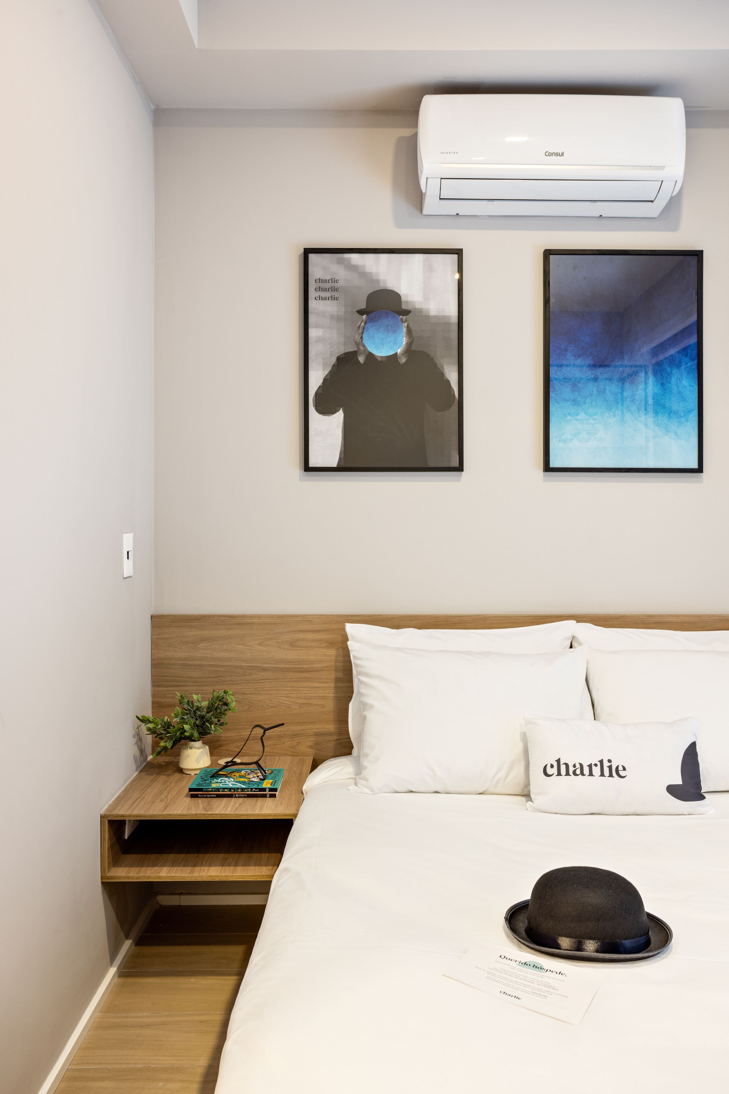 Ein Hotelzimmer mit einem Bett, einem Nachttisch, einer Wand-Klimaanlage und zwei gerahmten Bildern.