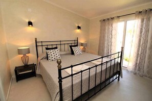 A bedroom with a bed, two bedside lamps, a nightstand, and a window with curtains. - Ocean View Apartment with Swimming pool at São Rafael Beach - Albufeira (Albufeira)