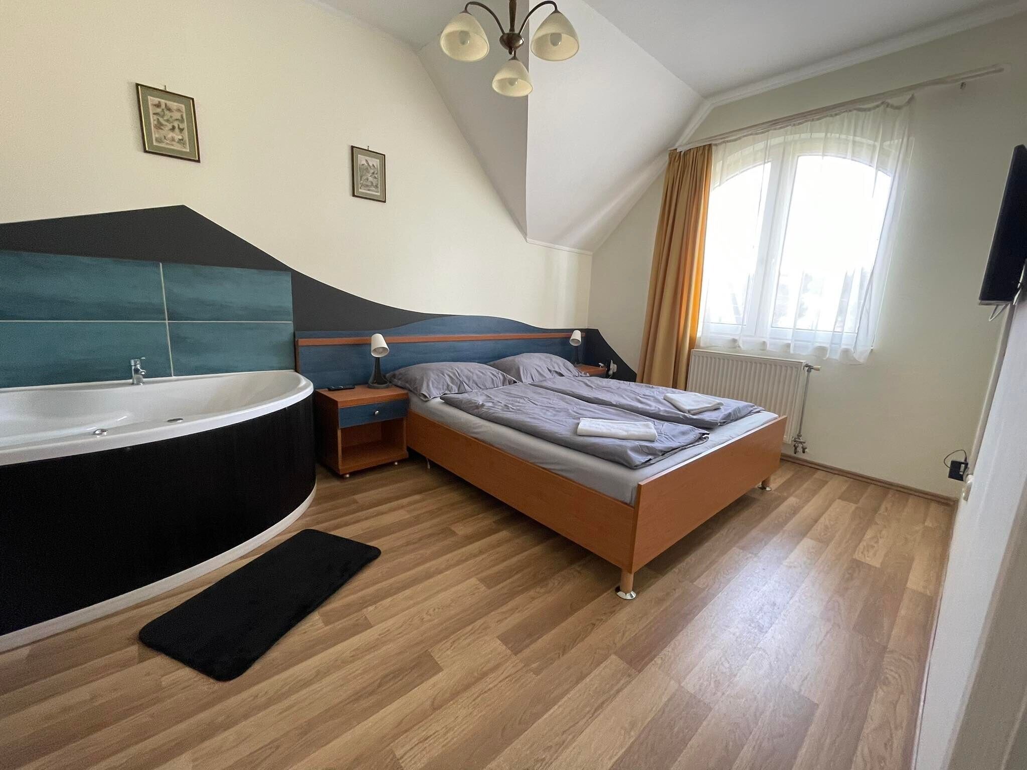 A bedroom with a large bathtub, a wooden bed, a nightstand, and a window with curtains.