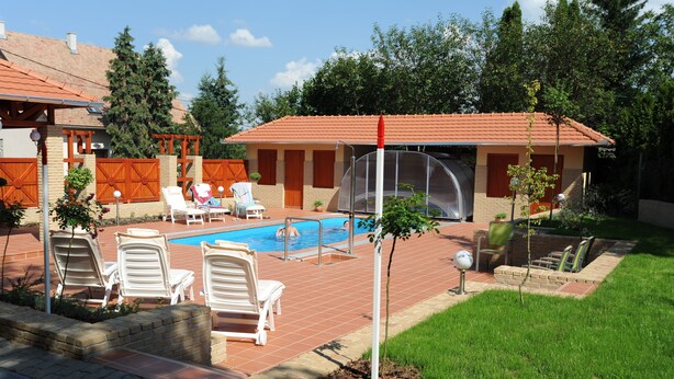 A backyard with a swimming pool, white lounge chairs, and a small tree. - Tölgyfa Panzió (Miskolc)