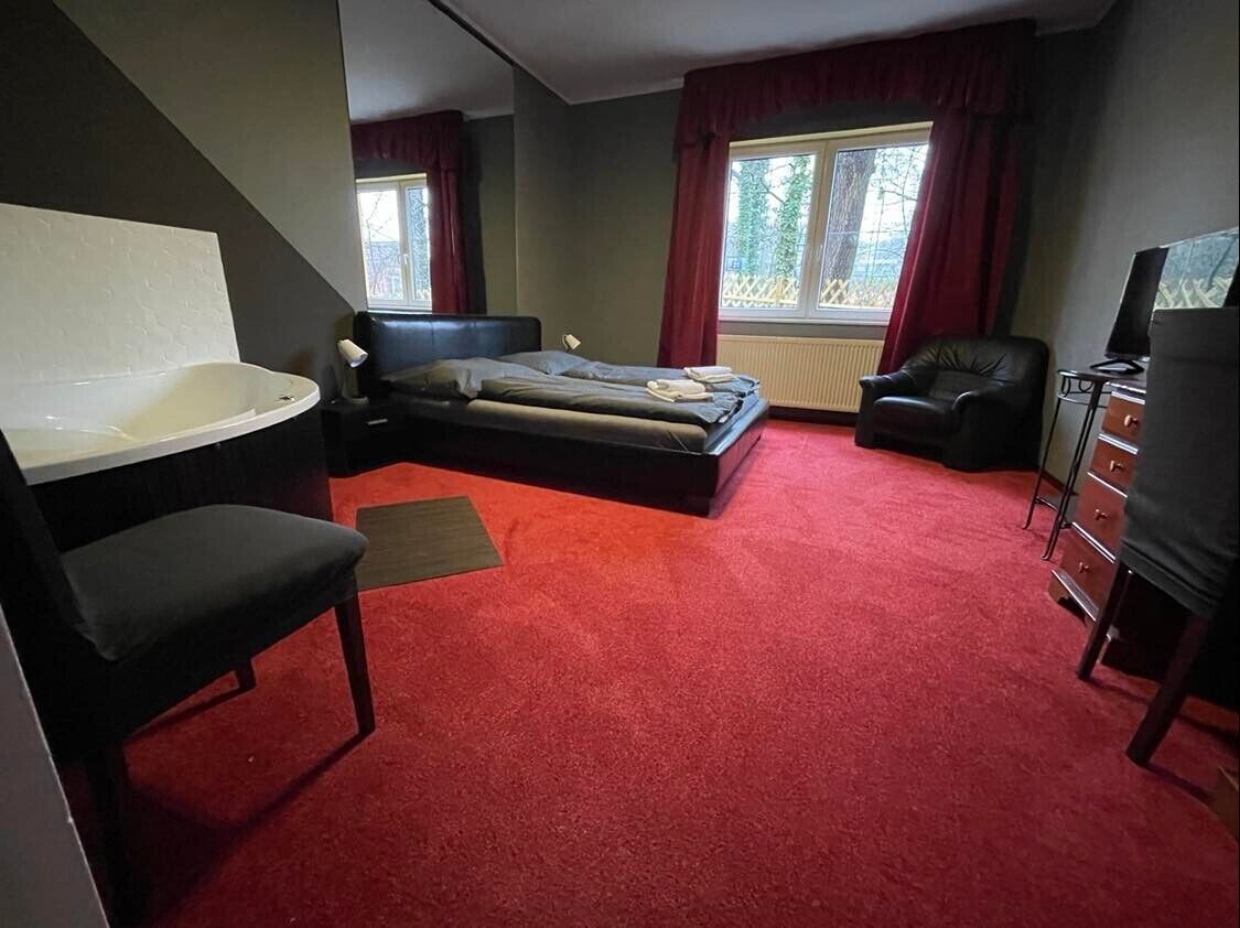 A bedroom with a large bed, a separate chair, a desk, and a bathtub.