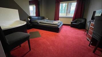A bedroom with a large bed, a separate chair, a desk, and a bathtub.