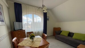 A dining area with a table set for two, a sofa, and a television on a cabinet. - Tölgyfa Panzió (Miskolc)