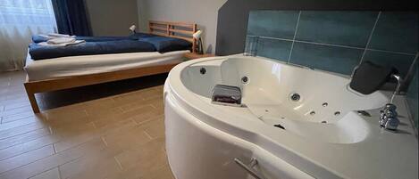 A modern bathroom with a large bathtub, a wooden bed, and a window with curtains.
