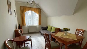 A dining area with a wooden table and chairs, a sofa, and a window with curtains. - Tölgyfa Panzió (Miskolc)