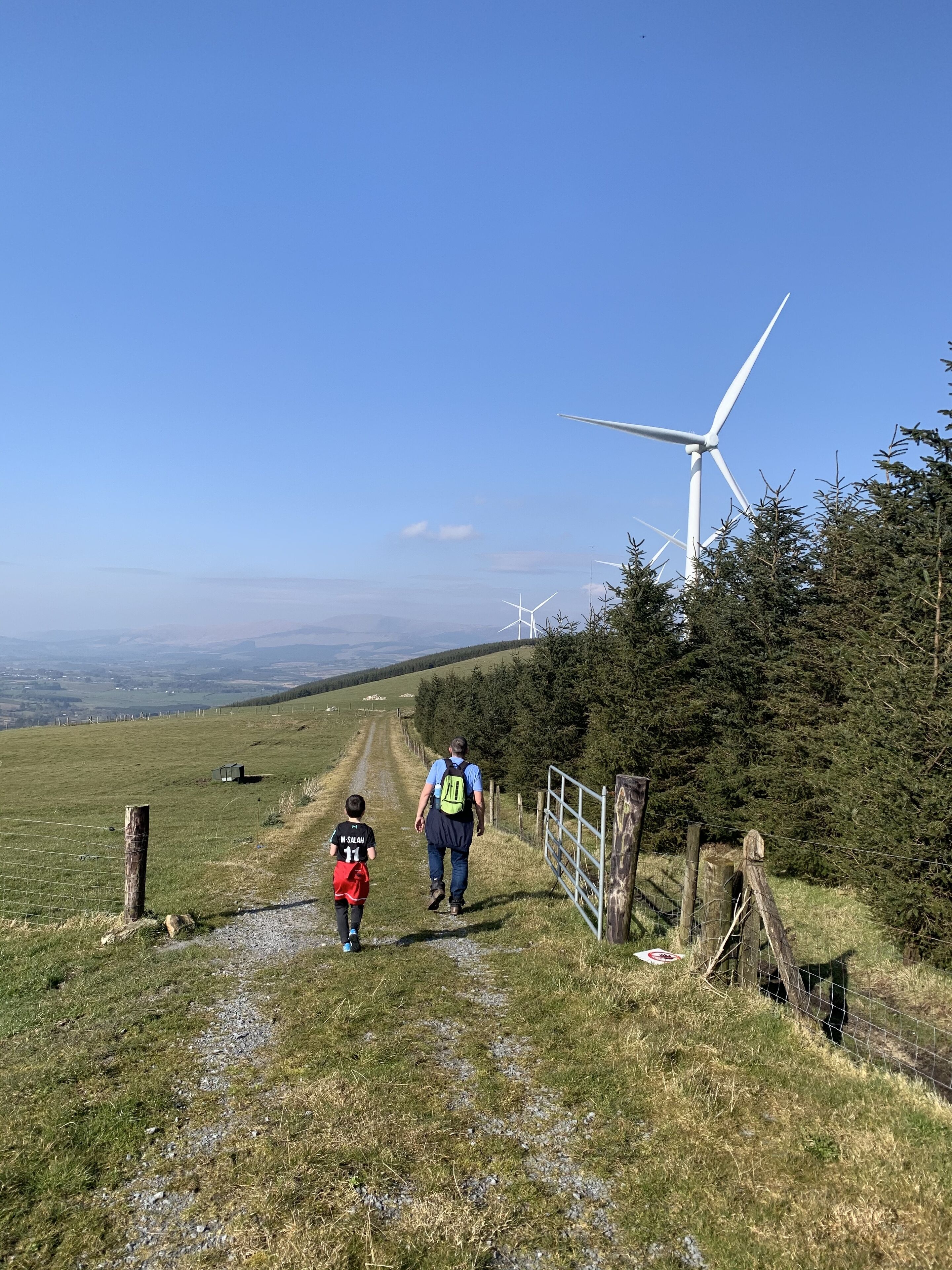 A pathway leading uphill with a wind turbine in the background.