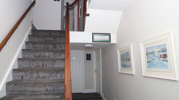 Un escalier avec une rampe en bois mène à une porte portant le numéro « 10 ». À côté de la porte, on trouve une enseigne indiquant « Modeline Accommodation ». Deux tableaux encadrés sont accrochés au mur.