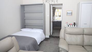 Una habitación de hotel con cama, sofá, armario y una mesita con artículos de aseo.