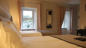 Una habitación de hotel con dos camas, una ventana con cortinas, un espejo y una mesita de noche con lámpara.