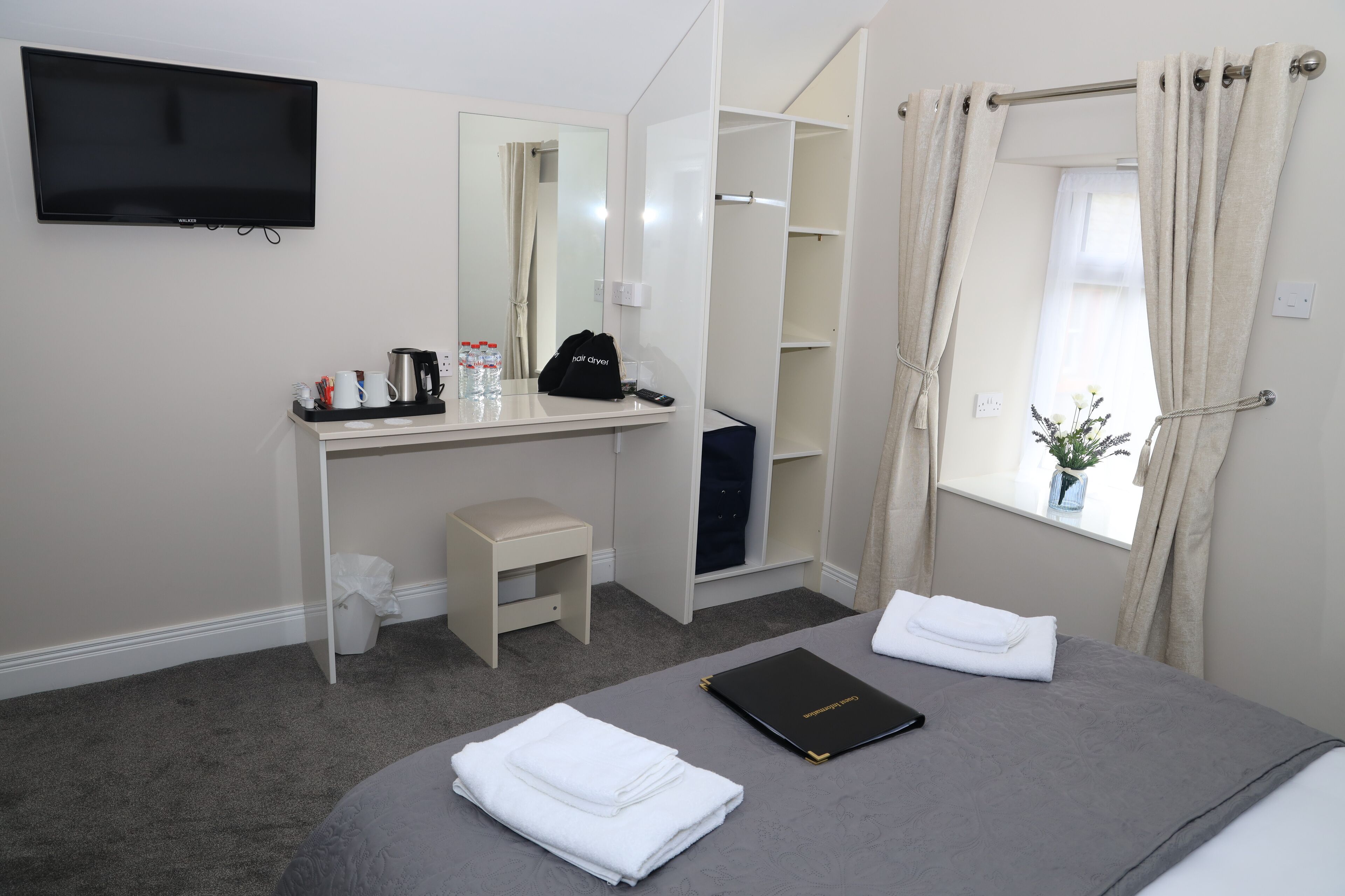 Habitación de hotel con cama, escritorio, silla, televisor, ventana con cortinas y una pequeña planta.
