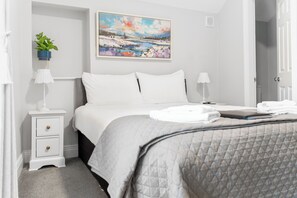 Un dormitorio ordenado con cama, mesitas de noche, una planta en la pared y un cuadro.