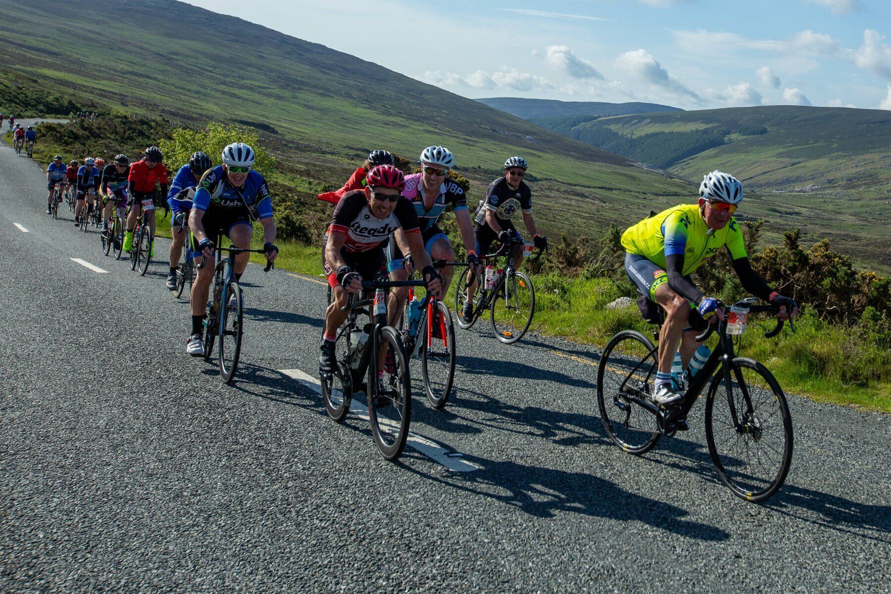 A group of cyclists on a road with a scenic mountainous backdrop.