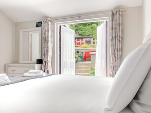 Habitación de hotel con cama, mesita de noche, espejo y ventana con cortinas.