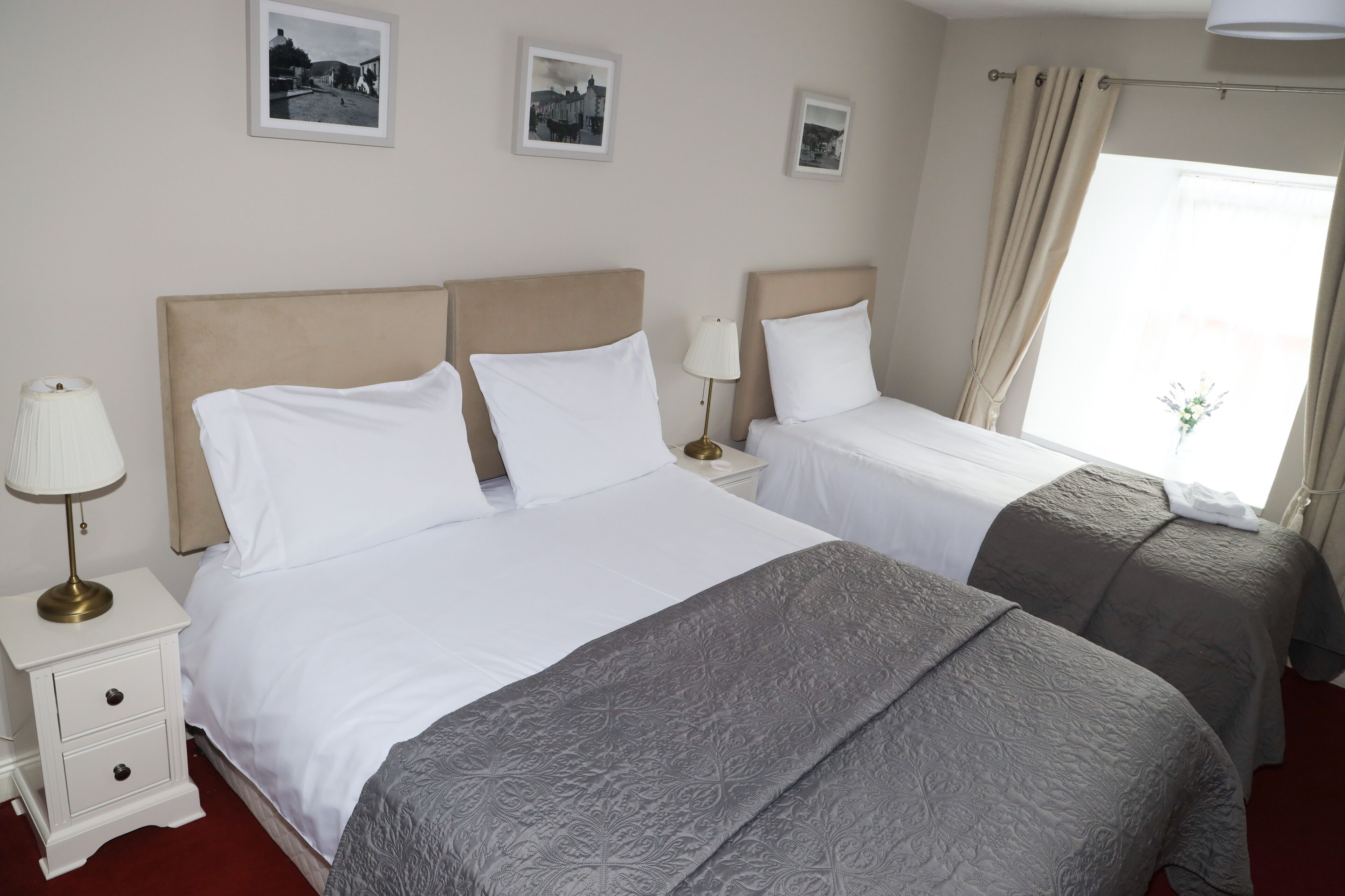 A hotel room with two beds, a nightstand with a lamp, and a window with curtains.