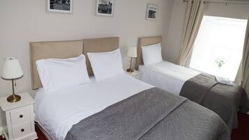 A hotel room with two beds, a nightstand with a lamp, and a window with curtains.