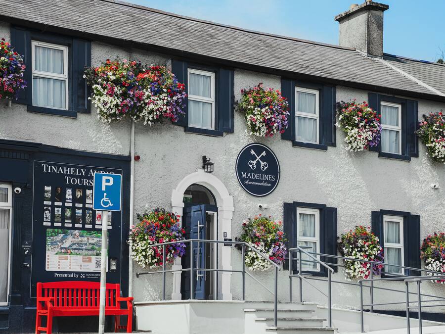 A building with multiple flower boxes on the windowsills, a sign for 'Madelines Accommodation,' and a wheelchair-accessible parking sign.