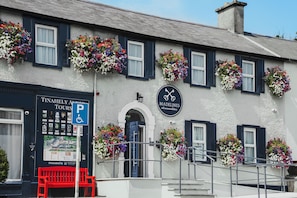 A building with multiple flower boxes on the windowsills, a sign for 'Madelines Accommodation,' and a wheelchair-accessible parking sign. - Madelines Accommodation (Tinahely)